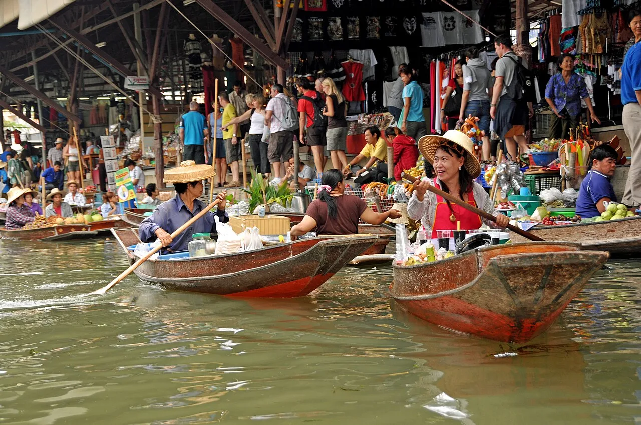 Vendors paddling boats at Damnoen Saduak floating market with tourists on the shore